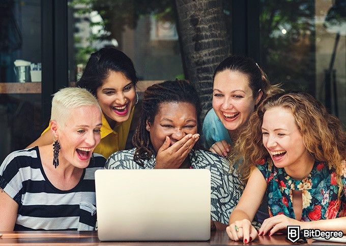 Online social sciences degree: five women are looking at a laptop screen and laughing.