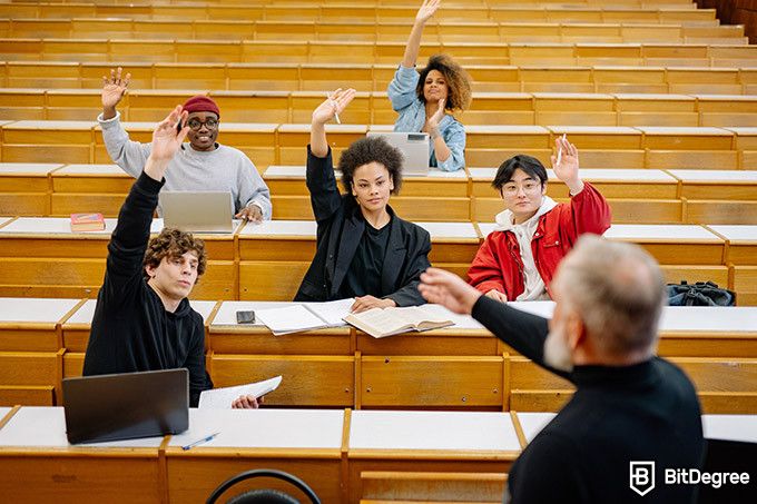Online teaching courses: students raising hands in the classroom.